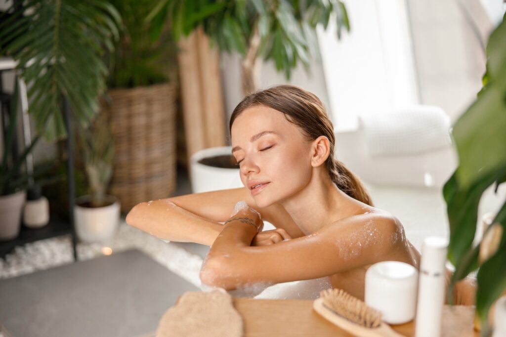 Relaxed young woman leaning on bathtub side while bathing with eyes closed at spa resort