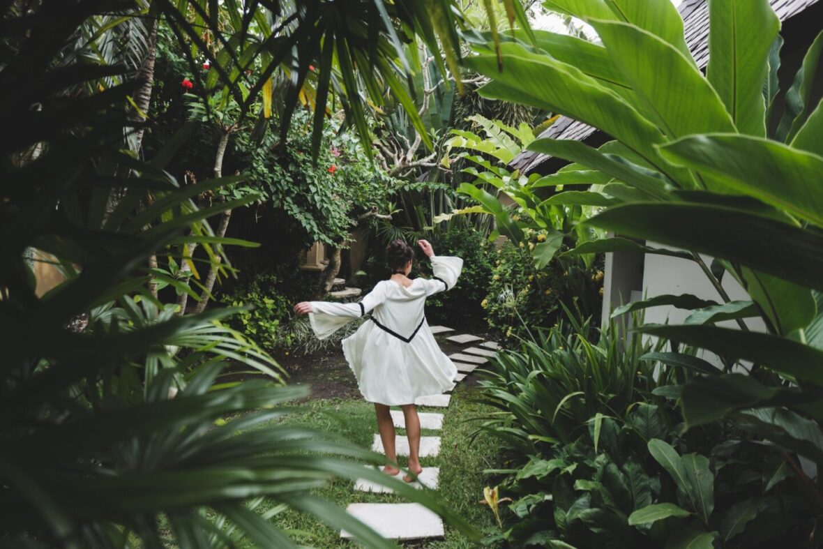 Woman walking in tropical garden in white dress. Brunette with long black hair. Fashion tunic