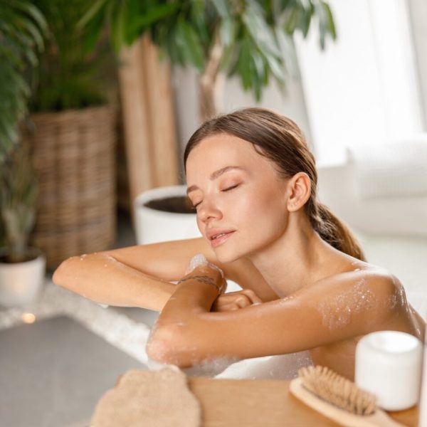 Relaxed young woman leaning on bathtub side while bathing with eyes closed at spa resort