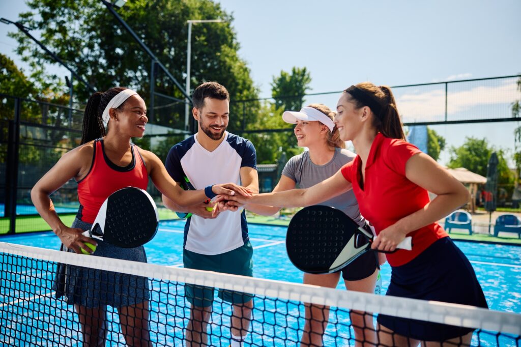 Happy paddle tennis players joining hands in unity while celebrating after the match.