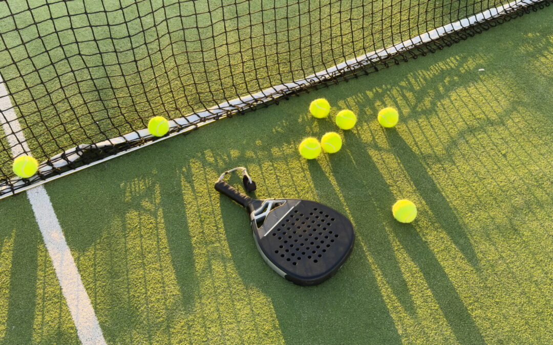 Padel racket and padel ball on a green court in the sunset