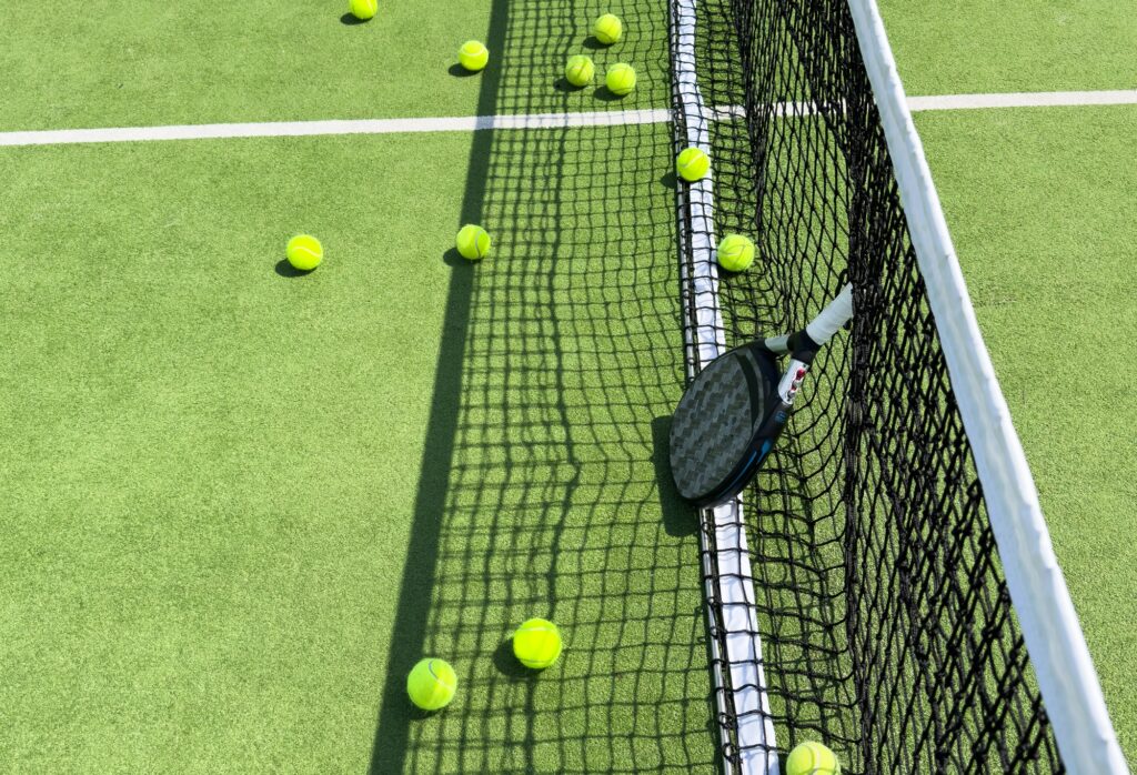 Padel racket and padel ball on a green court in the sunset