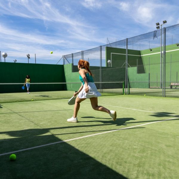 Two women playing padel on an outdoor court, one chasing the ball in mid-action.